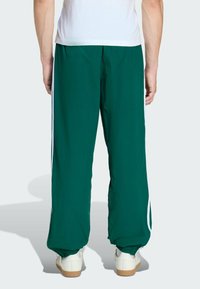 Zielone spodnie sportowe z białymi paskami po bokach, elastycznymi mankietami i lekkim materiałem. Oferują luźny krój i prosty design.