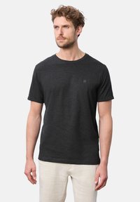 Svart t-shirt med kort ärm gjord av mjukt tyg, med rund halsringning och liten logotypdetalj på bröstet, matchad med ljusa byxor.