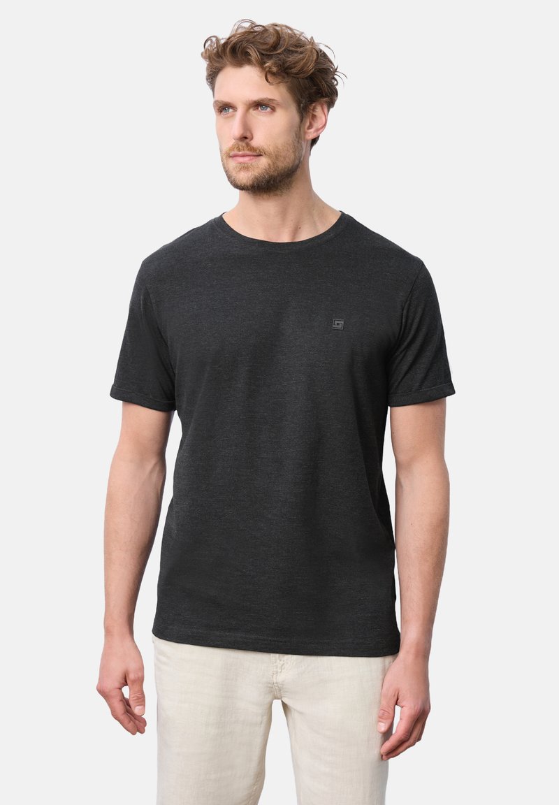 Svart t-shirt med kort ärm gjord av mjukt tyg, med rund halsringning och liten logotypdetalj på bröstet, matchad med ljusa byxor.