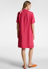 Abito in lino rosa con maniche corte, vestibilità ampia, tasche laterali e sciarpa a fiori al collo. Tessuto liscio, lunghezza fino a metà coscia.
