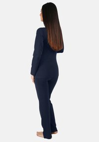 Dunkelblaues, langärmliges Oberteil und passende Hose, figurbetonter Stil, weicher Stoff und Standardlängenbeine, von hinten betrachtet.