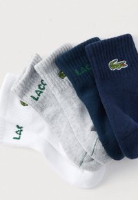 Σετ τριών ζευγαριών κάλτσες σε λευκό, γκρι και ναυτικό μπλε. Διαθέτουν ριμπ μανσέτες, απαλό υλικό και κεντημένο λογότυπο κροκόδειλου.
