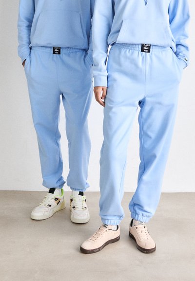Pantalons de survêtement bleu clair avec une taille élastique et des poignets, dotés de poches latérales. Associés à des baskets contrastantes dans des tons variés.