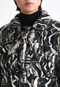 Faux fur jack in zwart, beige en bruin met een golvend dierenprintpatroon. Voorzien van een kraag en knoopsgaten op de borstzakken.