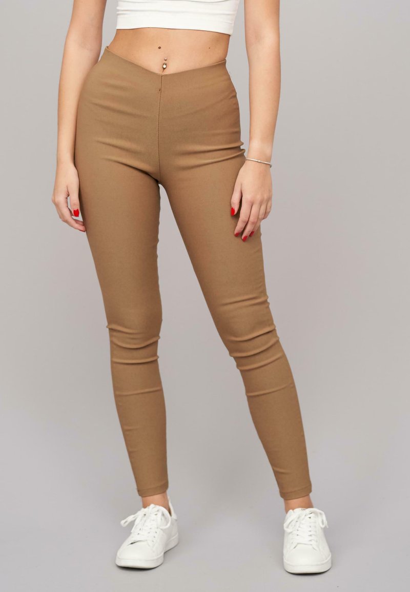 Barna, magas derekú leggings, rugalmas anyagból, sima textúrával és testhezálló kialakítással, fehér sportcipővel párosítva.