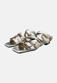 Sandali piatti argentati con più cinturini, caratterizzati da accenti metallici e una punta quadrata. Finitura testurizzata sui cinturini, chiusura con fibbia sicura.