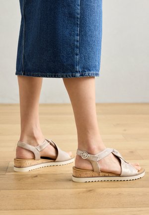 Sandalias de cuero beige con tacón de corcho y correa ajustable. Presentan un diseño superior entrelazado y una suela texturizada para mayor agarre.