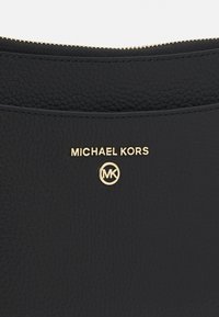 Sort læderhåndtaske med en struktureret overflade, guldfarvet logo "MICHAEL KORS" og emblem, samt en lynlås lukning langs den øverste kant.