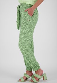 Pantaloni cu un model floral verde, cu talie legată, manșete elastice și buzunare laterale, asortați cu sandale verzi, decorate cu volane.