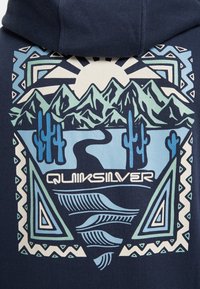 Sudadera azul marino con un gráfico geométrico. El diseño incluye montañas, cactus y un río en tonos de azul y verde con el texto "Quiksilver".