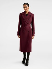 Burgundia kahekirjaline trench coat, millel on vööga talje, lõikega klapid, pikad varrukad ja küljetaskud, kombineeritud mustade sobivate pükste ja kontsaga kingadega.