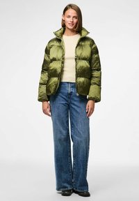 Alyvuogių spalvos pūkuota striukė su blizgiu paviršiumi, užtrauktuku ir aukštu apykakle. Pora su šviesiai mėlynomis plačiomis kelnėmis ir kreminės spalvos marškiniais.