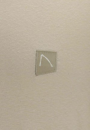 Beige-kangas, jossa on teksturoitu pinta, sisältää suorakulmaisen logo-patchin vaaleammassa beigenvässä, joka on painettu minimalistisella suunnittelulla valkoisena.