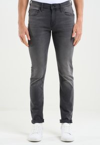Sive jeans iz denima z oprijeto prileganjem, petimi žepi in subtilnim zbledelostjo. Zasukani robovi in gladka tekstura. V kombinaciji z belimi teniskami.