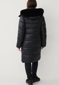 Lang, sort termojakke med en krave af kunstpels, der har syede vandrette paneler og en afslappet pasform, der går til midt på læggen.