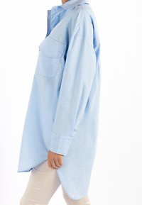 Camicia azzurra chiara con maniche lunghe, taschino frontale e orlo curvo. Realizzata in un tessuto liscio e leggero.