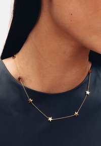 Ogrlica s privjeskom zlatne zvijezde i izmjenjujućim privjescima zvijezda na delikatnom lancu, postavljena na tamnoplavom kožnom vrhu.