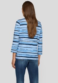 Blau gestreiftes Oberteil mit dreiviertel Ärmeln, das verschiedene Blautöne und weiße Linien auf einem weichen Stoff zeigt, kombiniert mit Jeans.