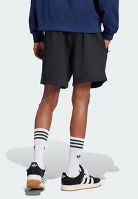 Schwarze Sportshorts, navyfarbener Sweatshirt, weiß gestreifte Socken und schwarz-weiße Sneaker mit Wildlederakzenten. Fokussierung auf lässige Passform und Stoffstruktur.
