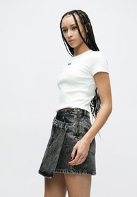 Fehér, rövid ujjú, testhezálló póló kék címkével; magas derekú fekete farmer szoknya egyedi cipzár- és hajtókafedél részlettel az elején.