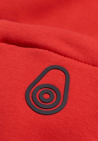 Červená tkanina má černé logo ve tvaru avokáda s koncentrovanými kruhy, které ukazuje hladkou strukturu a jednoduchý design.