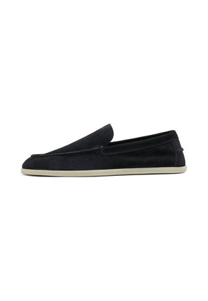 Mocassino nero in suede con suola in gomma beige, tacco basso, punta arrotondata e cuciture visibili lungo i bordi superiori.