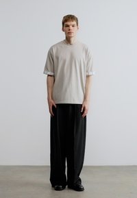 Hellgraues, übergroßes T-Shirt mit kurzen Ärmeln und hochgekrempelten Bündchen, kombiniert mit locker sitzenden schwarzen Hosen und schwarzen Schuhen.