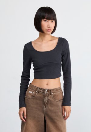 Zwarte lange mouw cropped top met een geribbelde textuur, voorzien van een brede ronde halslijn en subtiele naaddetails, gecombineerd met tan hoge taille broeken.