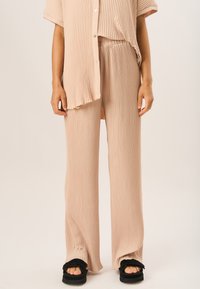 Beige ribbed knit two-piece set featuring a loose button-up shirt and elasticated waist pants. The fabric has a soft texture with subtle horizontal lines.