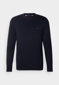 Pull à manches longues bleu marine avec col rond et petit logo rouge, blanc et bleu sur le côté gauche de la poitrine.
