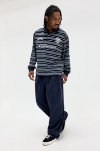 Polo de manga longa listrado em azul-marinho, com colarinho, combinado com calças largas em azul-marinho e sapatilhas verde-escuras. Acentos mínimos e logótipo.