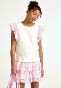 Hvid bomuldsbluse med pink spidstekantede flæseærmer, parret med en pink blomsterbroderet nederdel med lagdelt design og bølget kant.