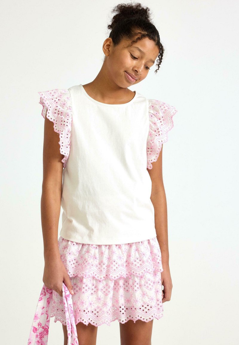 Hvid bomuldsbluse med pink spidstekantede flæseærmer, parret med en pink blomsterbroderet nederdel med lagdelt design og bølget kant.