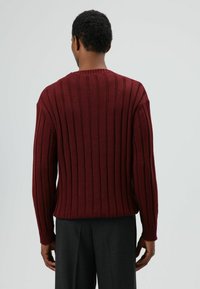 Dunkelroter, gerippter Pullover mit langen Ärmeln, rundem Ausschnitt sowie elastischen Bündchen und Saum. Rückansicht zeigt Struktur und vertikale Musterdetails.