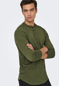 Olijfgroene long-sleeve henley shirt met een ronde hals, drieknopsbies en nauwsluitende mouwen, gemaakt van een gestructureerde stof.