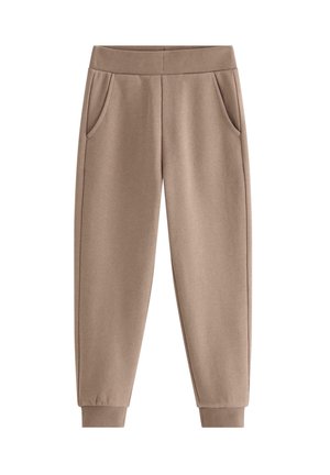 Barn iført brune joggingbukser, farverige stribede sokker og sølv- og hvide sneakers står på et lyst gulv.