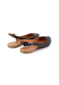 Zapatos de piel negra tipo slingback con puntera redonda, suela plana color marrón claro y detalle de hebilla plateada en la correa ajustable.