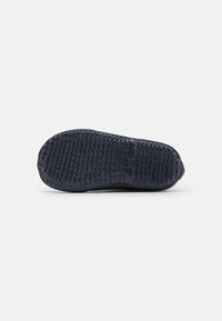 Semelle de sneaker en caoutchouc bleu marine foncé, texturée avec des rainures et des crêtes pour l'adhérence, présentant une légère courbe au talon et un bord lisse.