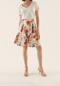 Blommig midi kjol i kräm med röda och blå blommor, i kombination med en vit t-shirt med V-krage och gyllene högklackade sandaler.