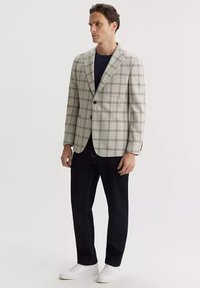 Jasnoszary marynarka w kratę z wyłogami, zapinana na jeden guzik, z kieszeniami z przodu, zestawiona z ciemnymi dżinsami i białymi sneakersami.