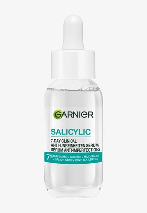 Bottiglia di vetro trasparente con tappo contagocce bianco. L'etichetta presenta testo verde e turchese. Contiene un siero trasparente con bolle visibili.