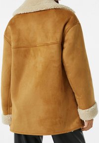 Hnědá faux semišová bunda s krémovým límcem a manžetami z faux kožešiny; má uvolněný střih a šev přes záda.