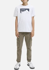T-shirt blanc à manches courtes avec un graphique de montagne, associé à un pantalon cargo vert olive avec des poches latérales et une coupe décontractée.