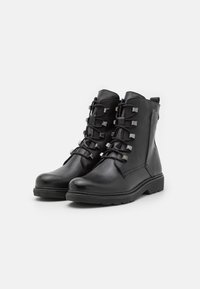 Botas de cuero negro hasta el tobillo con diseño de cordones y acentos metálicos, suela resistente y un acabado liso y texturizado.