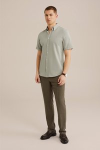 Camicia verde chiaro a maniche corte con colletto button-down, abbinata a pantaloni slim verde scuro e mocassini neri. Design semplice e pulito.