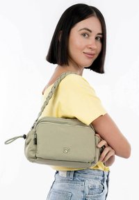 Borsa a spalla verde khaki con una tracolla intrecciata, scomparto con zip e superficie testurizzata. Presenta un logo argento sul fronte.