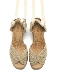 Sandales ouvertes beige à bout carré avec une tige en textile tressé, des perles décoratives et des sangles en tissu doux pour un maintien sécurisé. Semelle intérieure en cuir avec motif de feuilles.