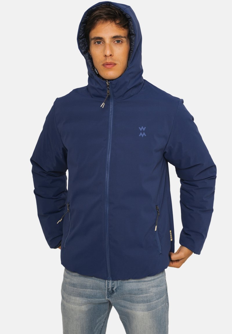 Veste zippée bleu marine avec une capuche, dotée de poches latérales et d'un logo. Le tissu semble lisse et léger avec un design simple.