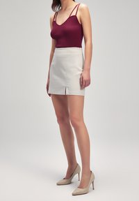 Burgunderröd randig tanktop med tunna axelband, kombinerad med en vit minikjol med en framfick, kompletterad med beige högklackade skor.