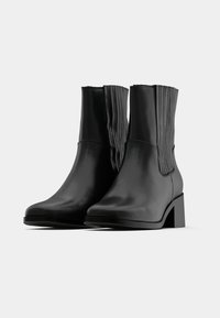 Černé kotníkové boty z hladké kůže s vertikálními žebrovanými detaily na bocích a blokovým podpatkem pro stabilitu.